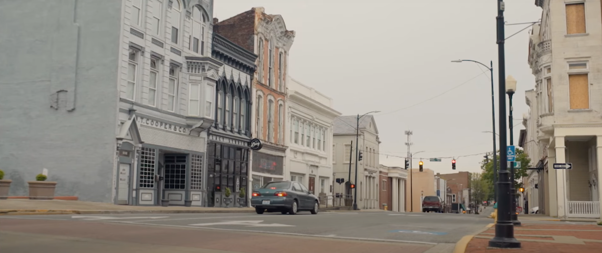 A car on a street coming to a stop light near older buildings of the town.